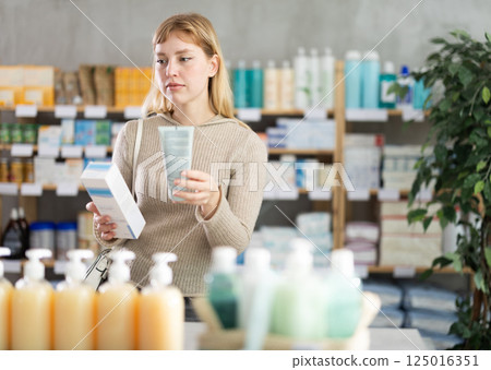 Young woman customer choosing cream in drugstore 125016351