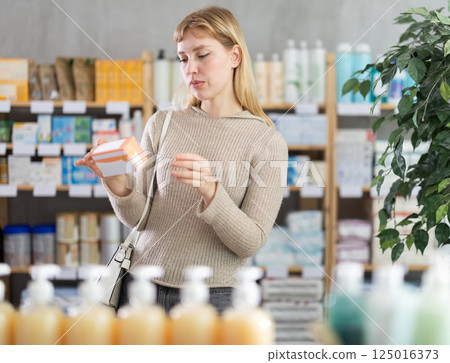 Girl in winter clothes looking for medicine in pharmacy 125016373