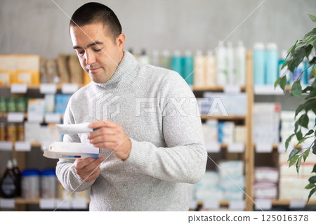 Young man chooses ointment at pharmacy 125016378