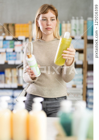 Female shopper in autumn clothes chooses medicated shampoo at pharmacy 125016399