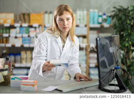 female pharmacist offers customers a pack of tablets in a pharmacy 125016413