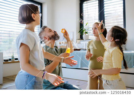 Portrait of father with three daughters blowing bubbles. 125016430