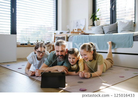 Portrait of father with three daughters watching tv show on tablet. Portrait of father with three daughters watching tv show on tablet. 125016433