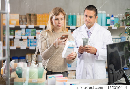 Woman scanning barcode of cream package with pharmacist in front of 125016444