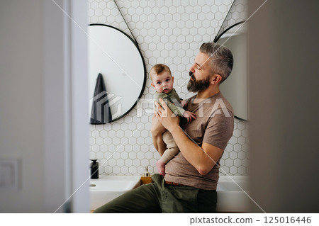 Portrait of father holding baby son in arms. 125016446