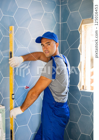 Smiling worker measuring wall with spirit level in new apartment 125016453