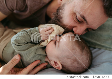 Father putting the baby to sleep, lying next to him in the crib. 125016454