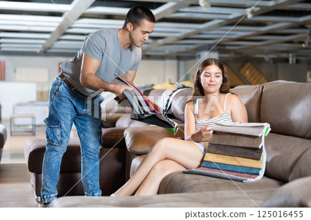 Woman is sitting on sofa and sales consultant shows her set of upholstery fabrics 125016455
