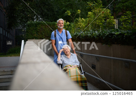 Male caregiver pushing senior woman in wheelchair. 125016465