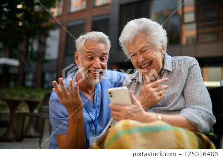 Male caregiver looking at photos with senior woman in wheelchair. Male caregiver looking at photos with senior woman in wheelchair. 125016480