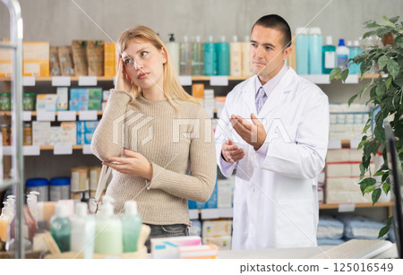 Young woman having headache while pharmacist offering in drugstore Young woman having headache while pharmacist offering in drugstore 125016549