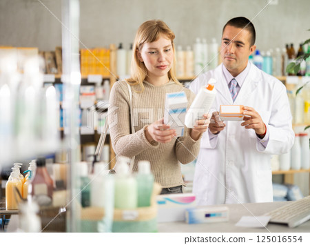 Young woman choosing cream while pharmacist offering in drugstore 125016554