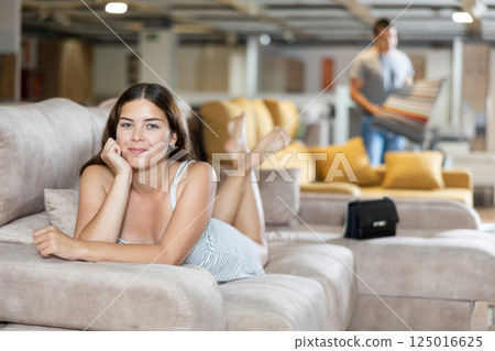 On sofa girl is lying on stomach with chin propped up in hands in furniture store 125016625