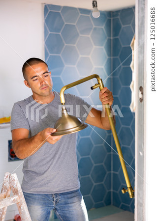 Professional handyman working in bathroom holding shower head indoors Professional handyman working in bathroom holding shower head indoors 125016688