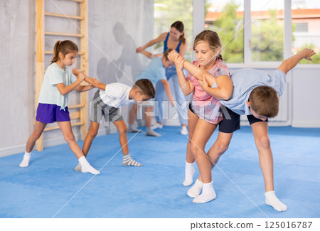 Children practicing in pair self-defence movements with female trainer supervision 125016787