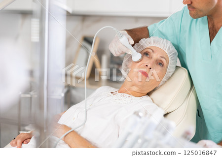 Experienced male cosmetologist performing female face skin massage procedure in clinic 125016847