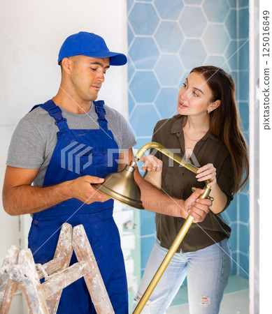 Plumber installing shower for woman in apartment Plumber installing shower for woman in apartment 125016849