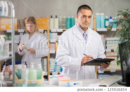 Young male pharmacist making notes on tablet for restocking in chemistry 125016854