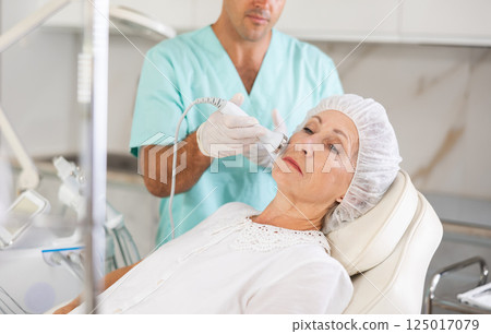 Experienced male cosmetologist performing female face skin massage procedure in clinic 125017079