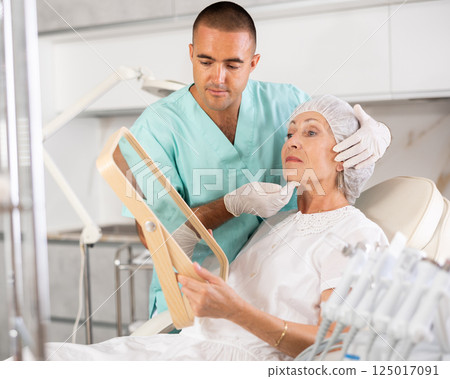 Man beautician examining face skin of female patient after cosmetology procedure in clinic 125017091