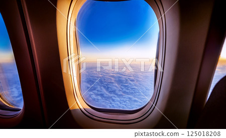 view from airplane window, inside an airplane, the window at the wing and a vast expanse of fluffy white clouds under a clear blue sky during daytime, looking out airplane, flying above clouds 125018208