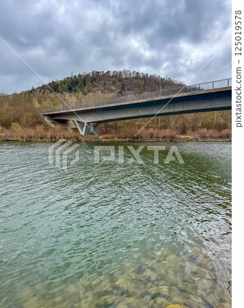 Modern bridge with steel supports crossing wide river and forested hillside. High quality photo Modern bridge with steel supports crossing wide river and forested hillside. High quality photo 125019578