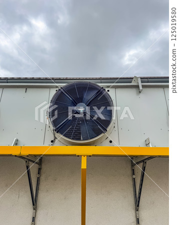 Large industrial ventilation fan mounted on building wall under cloudy sky. High quality photo 125019580