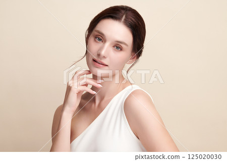 A beautiful young woman with clean, fresh skin against a beige background. Skincare, facial treatment, cosmetology, beauty, and spa. An elegant portrait of an woman. 125020030