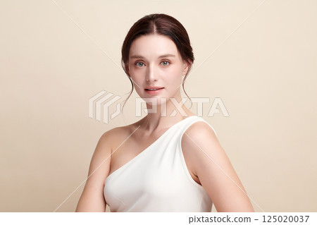 A beautiful young woman with clean, fresh skin against a beige background. Skincare, facial treatment, cosmetology, beauty, and spa. An elegant portrait of an woman. 125020037