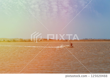 A man, an athlete, rides kitersurfing on a blue pore. Beach, active recreation. Sunset competitions, parachute, board. High quality photo A man, an athlete, rides kitersurfing on a blue pore. Beach, active recreation. Sunset competitions, parachute, board. High quality photo 125020488