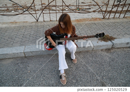 Girl Plays The Bass Instrument Sitting On The Step Near The Street At Evening 125020529