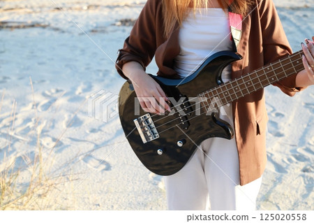 Girl Plays Bass Music Instrument On The Beach At Sunset Near Ocean Girl Plays Bass Music Instrument On The Beach At Sunset Near Ocean 125020558