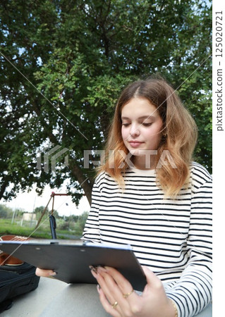 Girl Writes Notes On A Sheet Music To Play Them With The Ukulele 125020721