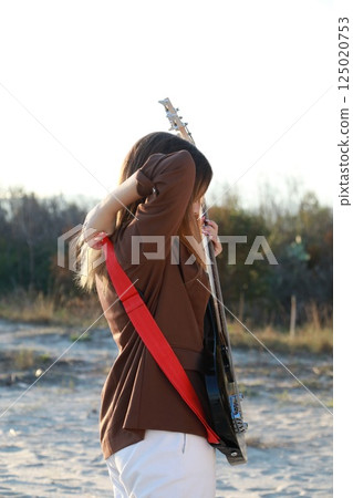 Girl Plays Bass Music Instrument On The Beach At Sunset Near Ocean Girl Plays Bass Music Instrument On The Beach At Sunset Near Ocean 125020753
