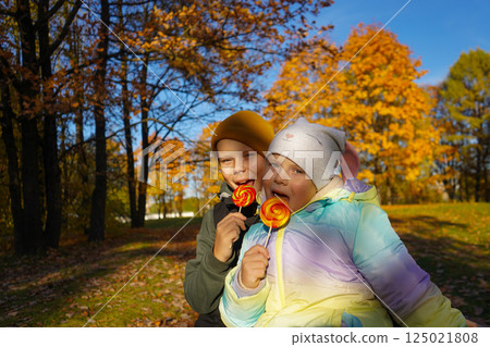 Portrait of a boy and a girl eating lollipops in an autumn park. 125021808