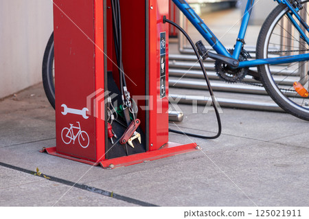 Public red bicycle repair station with tools and air pump beside parked blue bike on pavement Public red bicycle repair station with tools and air pump beside parked blue bike on pavement 125021911