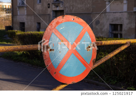 Rusty no stopping road sign mounted on metal barrier in residential area under afternoon sunlight Rusty no stopping road sign mounted on metal barrier in residential area under afternoon sunlight 125021917