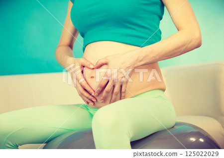 Pregnant woman making heart shape on belly with hands Pregnant woman making heart shape on belly with hands 125022029