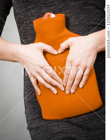 Girl holds hot water bottle on belly making heart shape by hands 125022034