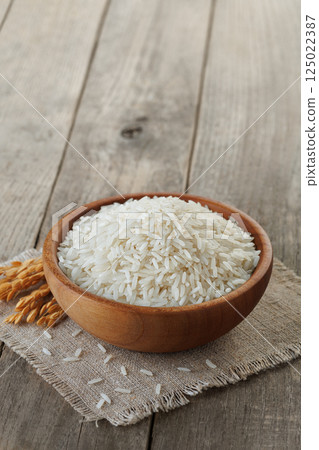 White rice fills wooden bowl standing on rustic table, accompanied by sprig of stalks 125022387