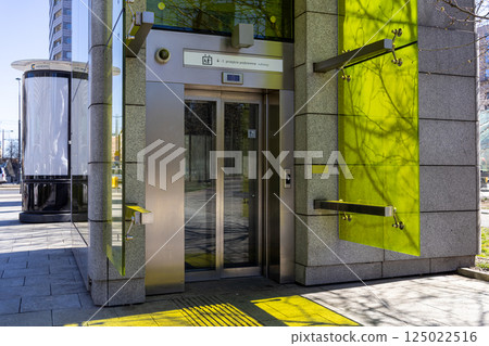 Glass elevator to underground pedestrian subway with green glass panels and tactile paving in modern city environment 125022516
