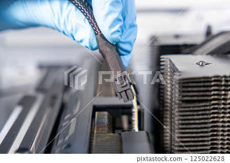 Technician in blue gloves holding 12VHPWR PCIe power cable above graphics card slot during PC assembly or GPU installation process Technician in blue gloves holding 12VHPWR PCIe power cable above graphics card slot during PC assembly or GPU installation process 125022628