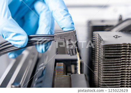 Technician in blue gloves positioning angled 16-pin PCIe power cable near graphics card socket during desktop PC hardware installation 125022629