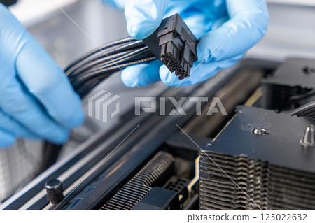 Technician in blue gloves holding 16-pin GPU power cable above graphics card inside custom-built desktop PC during installation process Technician in blue gloves holding 16-pin GPU power cable above graphics card inside custom-built desktop PC during installation process 125022632