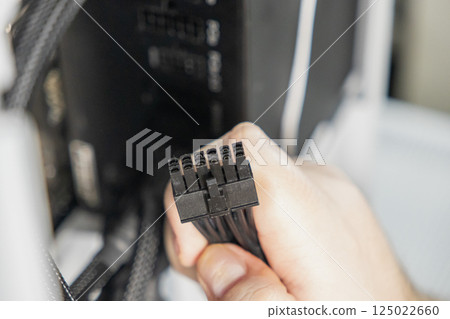 Close-up of technician holding black 8-pin power connector for motherboard or GPU during computer assembly inside PC case 125022660