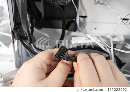 Technician connecting black SATA power cable inside computer case during PC build or hardware installation with visible wiring and components 125022662