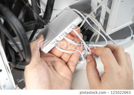 A technicians hands are connecting white LED cables to an RGB controller inside a PC case. The image captures a stage of assembling or upgrading internal lighting 125022663