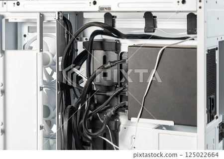 Close-up of cable management and power supply unit inside white open computer case with cooling fans during PC building or hardware installation 125022664