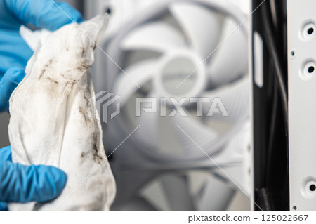 Technician in blue gloves holding dirty cleaning cloth in front of white computer cooling fan during PC maintenance process 125022667