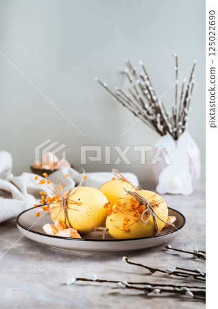 Easter decorations, decorated eggs on a plate, bunny and pussy willow on the table vertical view 125022690